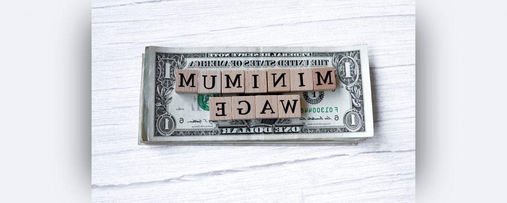 一张一美元钞票的图像，上面有拼字块，拼出了最低工资